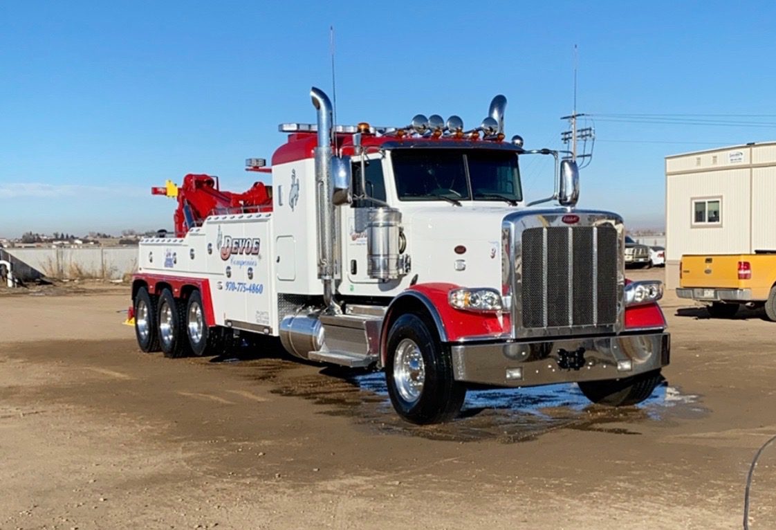 Heavy-duty white and red tow truck parked on dirt ground.